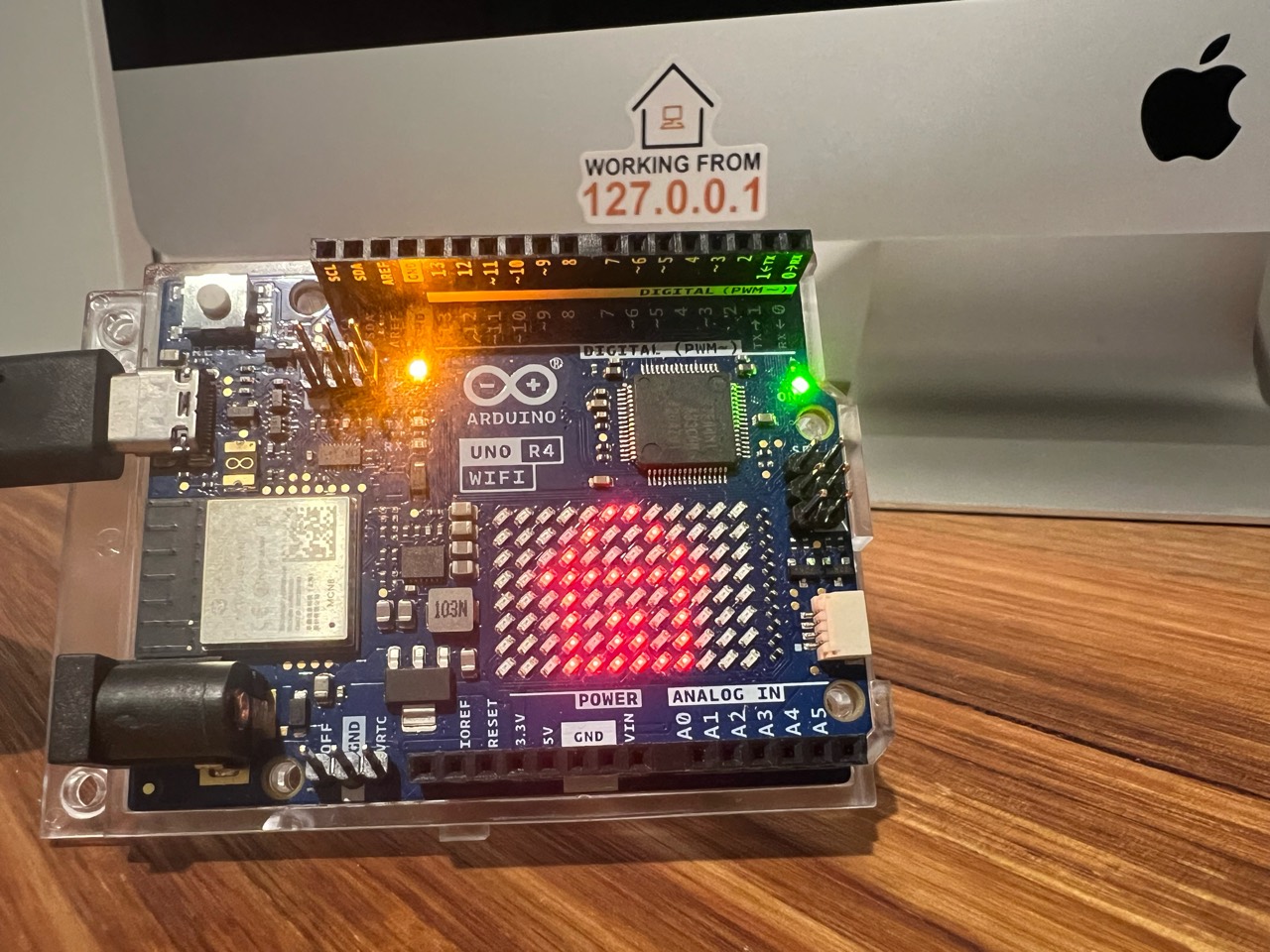 Arduino UNO R4 WiFi powered over USB on a desk, with its onboard LED and red LED matrix illuminated