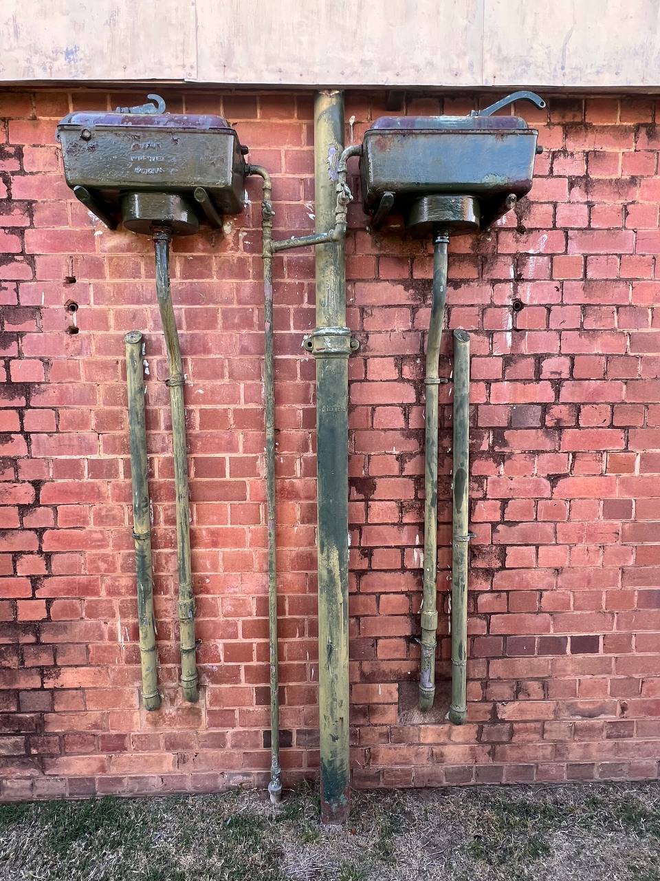 Vintage cast iron toilet cisterns mounted on a brick wall at the Old Dubbo Gaol