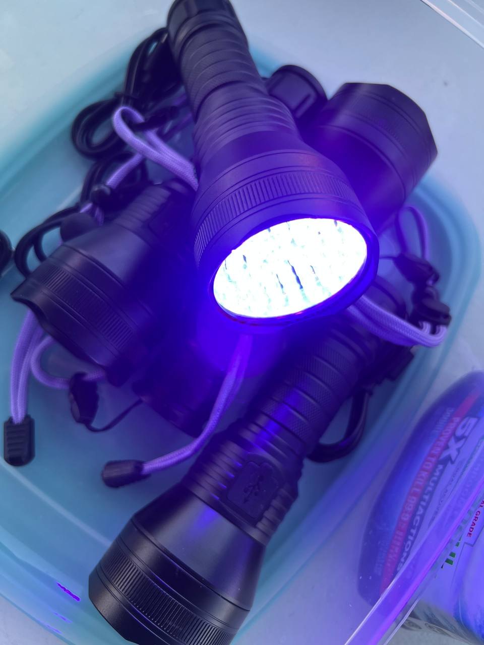 A container of rechargeable UV torches, one glowing