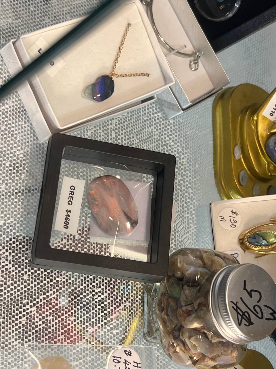 A stall table of opal jewellery and polished stones, including a large framed stone priced at $4,600 and $5 jars of opal chips