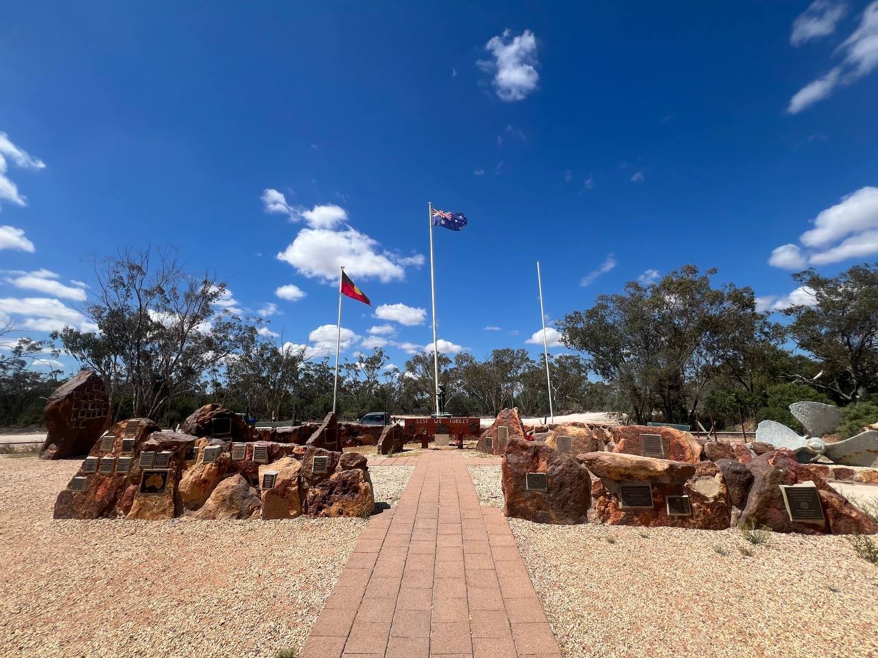 The Sheepyard and Community War Memorial: ironstone rocks with plaques, three flagpoles, and a propeller mounted at the right